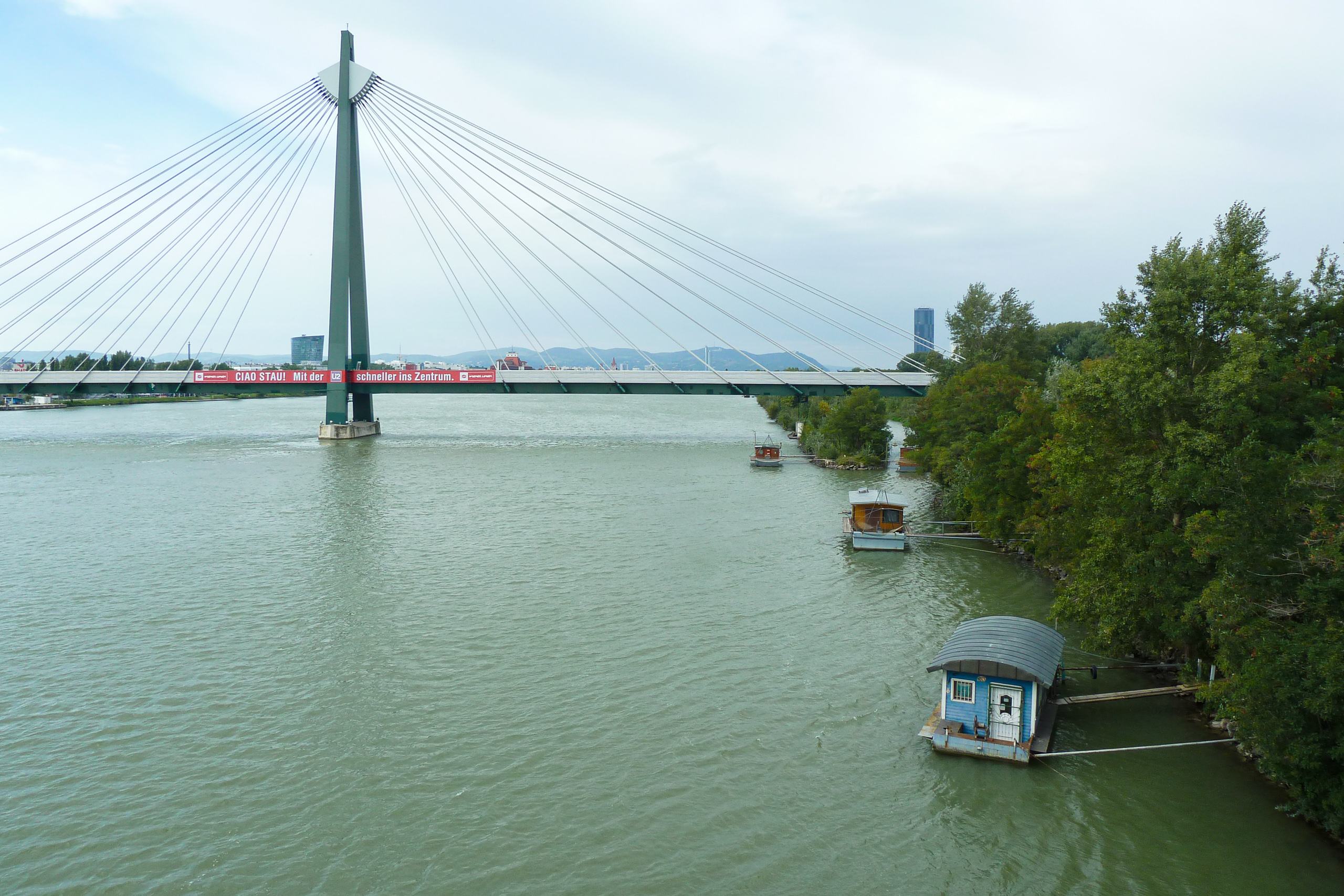 Schrägseilbrücke über die Donau, mit Hausbooten am Ufer